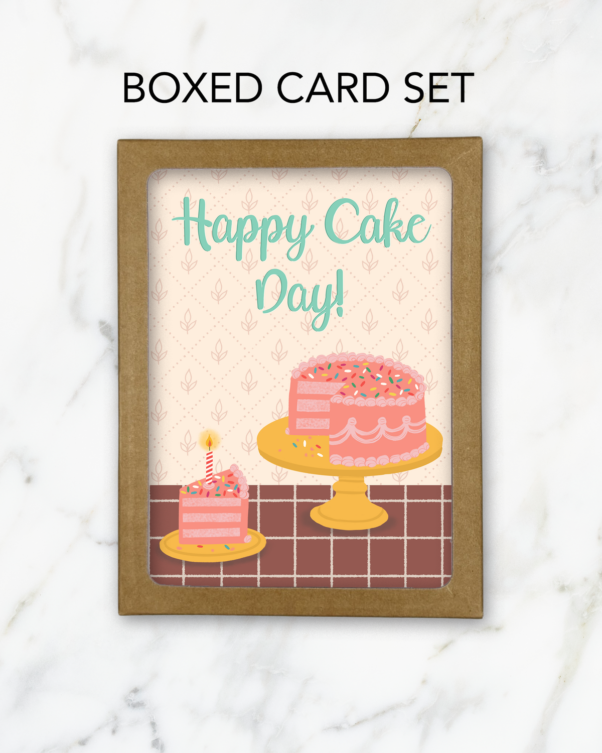 A kraft box with a cutout window showing greeting cards with a birthday cake illustration and the words Happy Cake Day! on a marble background
