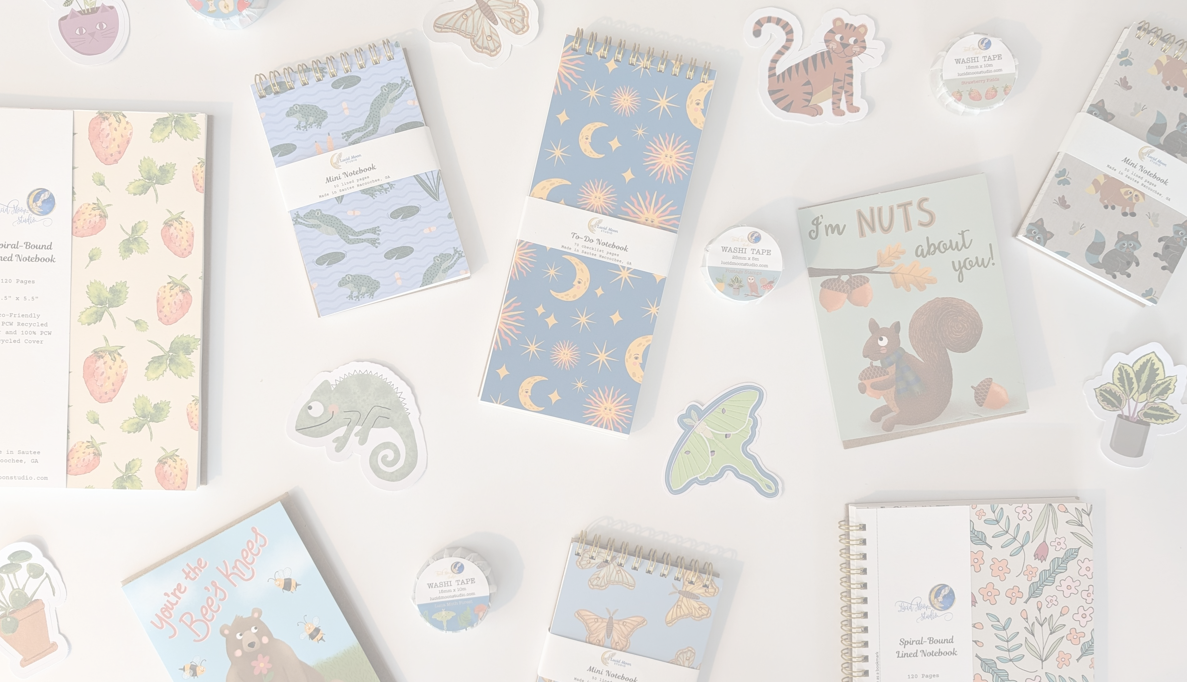 A photo of a variety of Lucid Moon Studio products including spiral-bound notebooks, jotters, greeting cards, washi tape, and stickers with whimsical designs drawn by Lisa Petrillo.