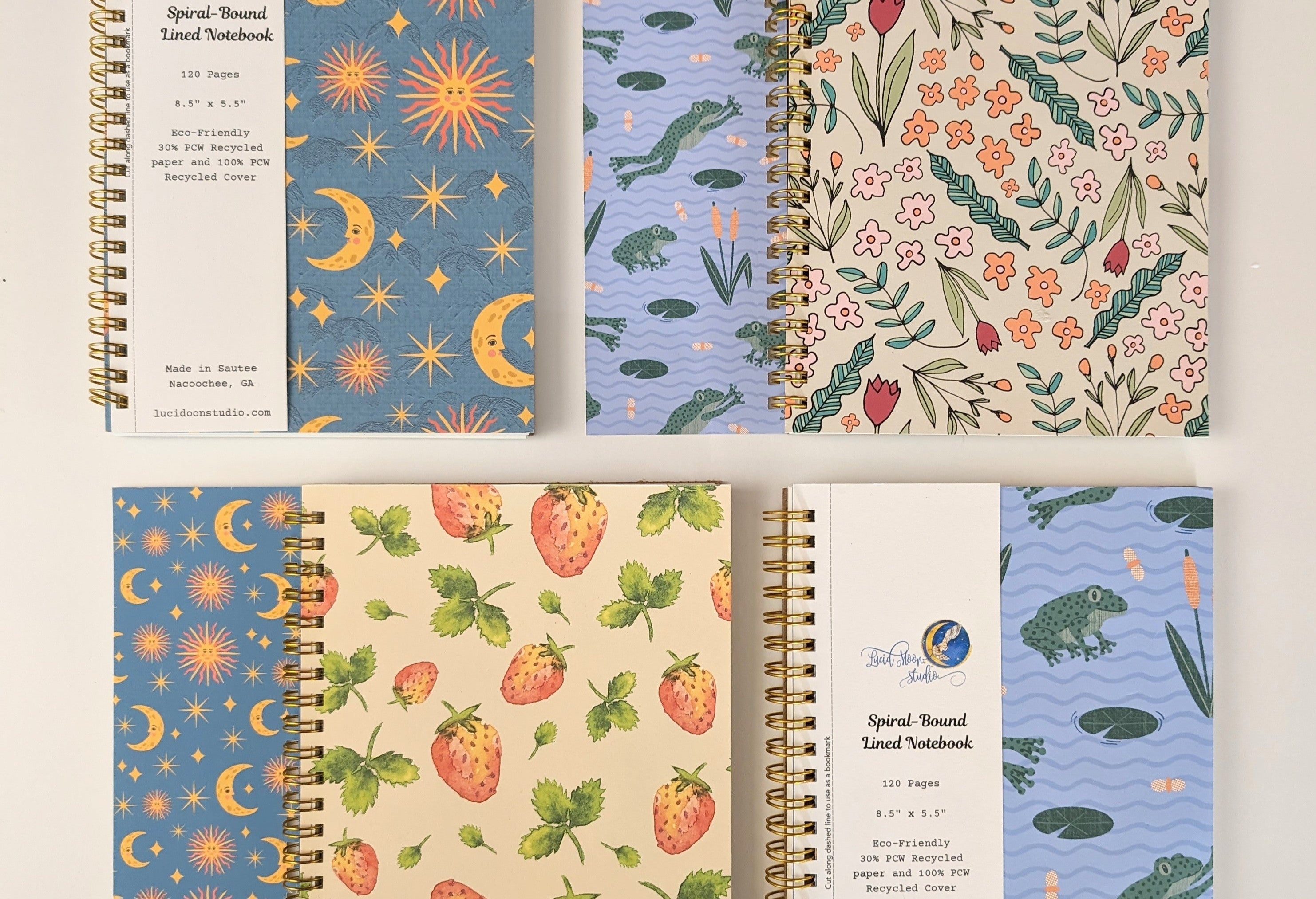 Four spiral-bound lined notebooks featuring strawberry, frog, sun and moon, and flower patterns on the covers and removable bookmark labels.