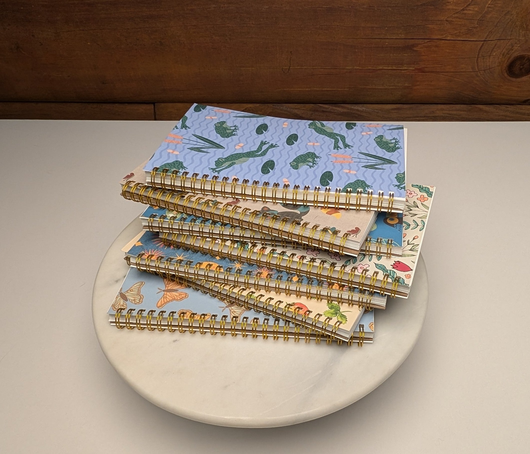 A stack of colorful wire spiral bound notebooks featuring heavy lined sheets and hand-drawn illustrations on the covers.