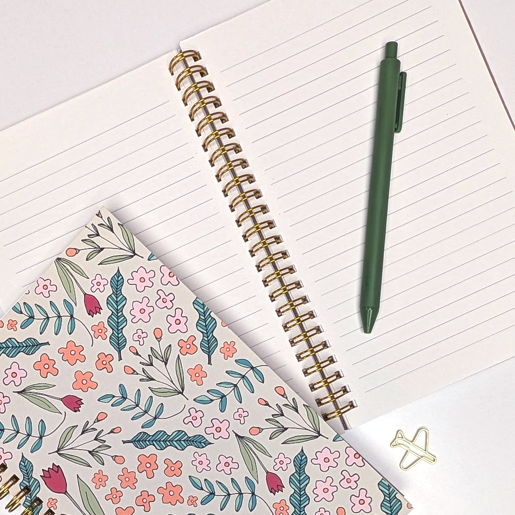 Notebook with floral cover, spiral binding, and green pen on a white surface