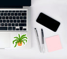 Vinyl matte die cut sticker with a hand drawn illustration of a green crocodile fern plant in an orange terracotta pot against a white background on a laptop with a phone, pens, and notepad.