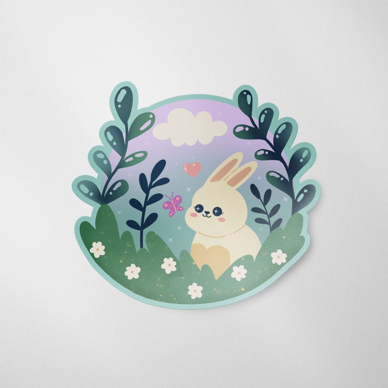 A hand-drawn matte die cut vinyl sticker featuring a cute Kawaii bunny sitting in a meadow surrounded by leaves, flowers, a pink butterfly, a heart, and a cloud in the background.