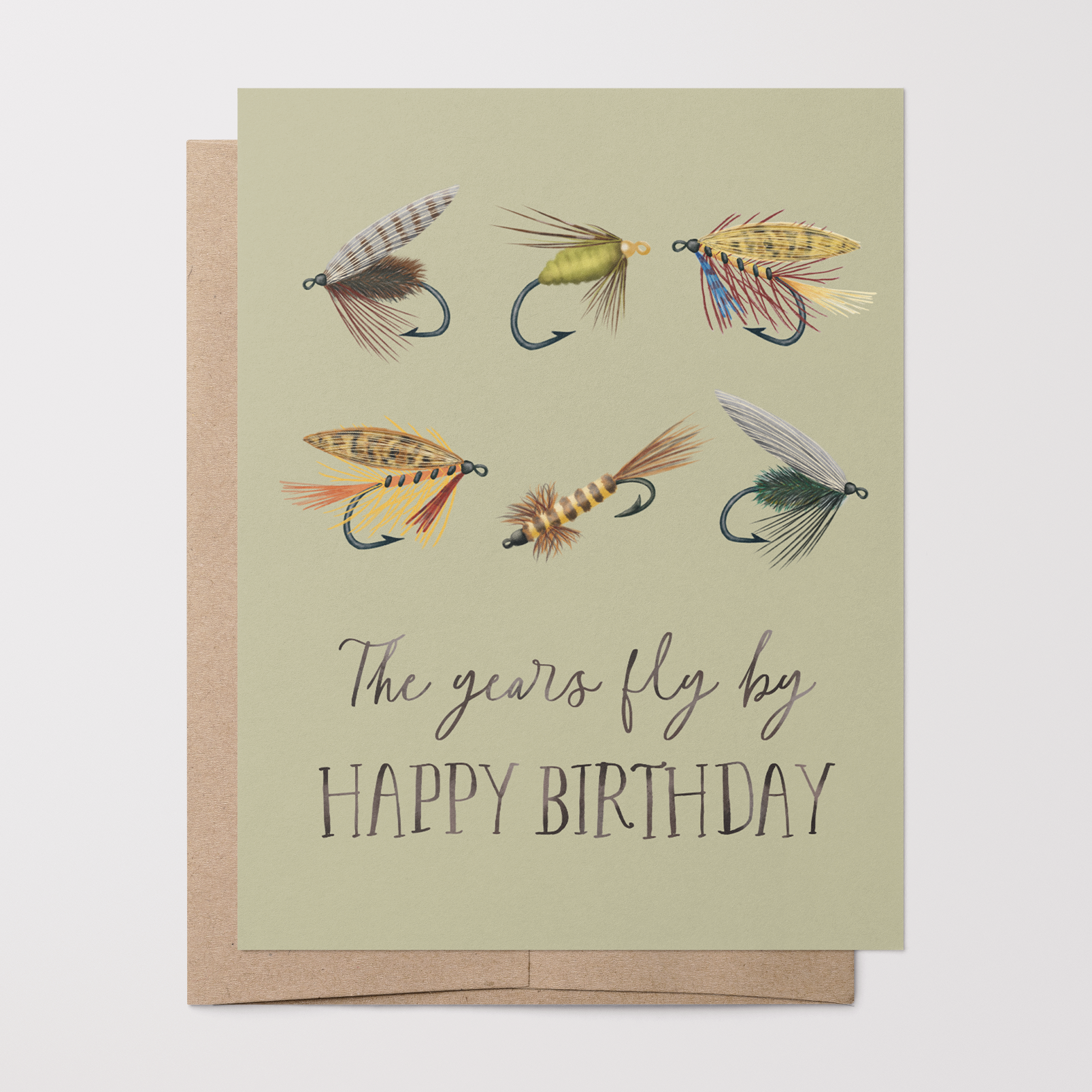 Birthday card with 6 fishing fly illustrations and text "The years fly by HAPPY BIRTHDAY" on a light green background on top of a brown kraft envelope.