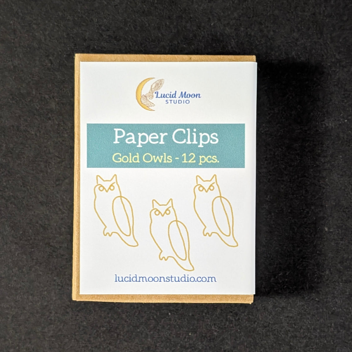 A small rectangular box of paper clips from Lucid Moon Studio, labeled 'Paper Clips Gold Owls - 12 pcs', placed on a dark textured background.