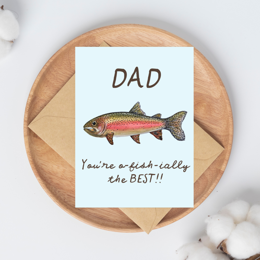 Greeting card with a watercolor rainbow trout illustration and the text "Dad You're o-fish-ially the BEST" on a light blue background on top of a brown kraft envelope.