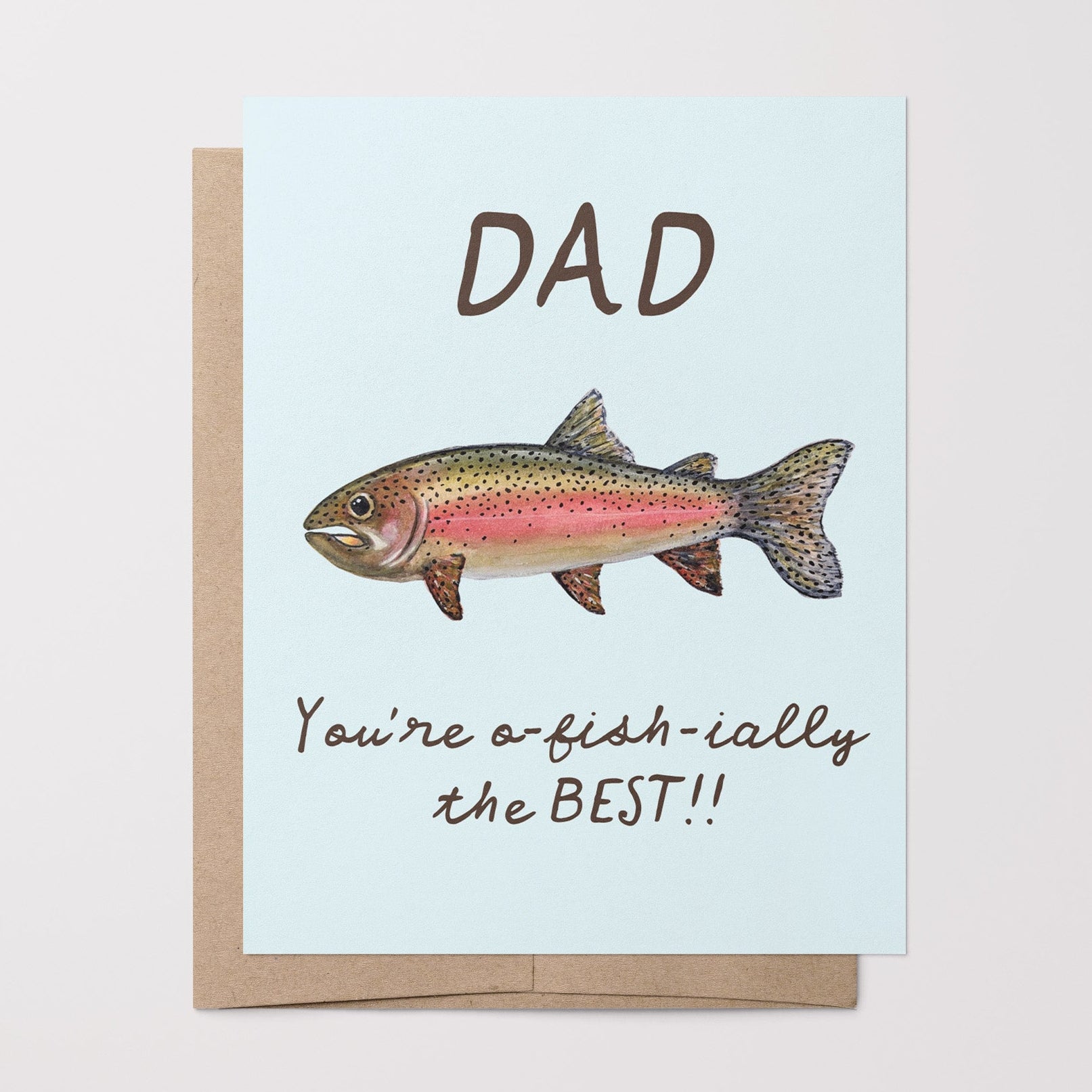 Greeting card with a watercolor rainbow trout illustration and the text "Dad You're o-fish-ially the BEST" on a light blue background on top of a brown kraft envelope.