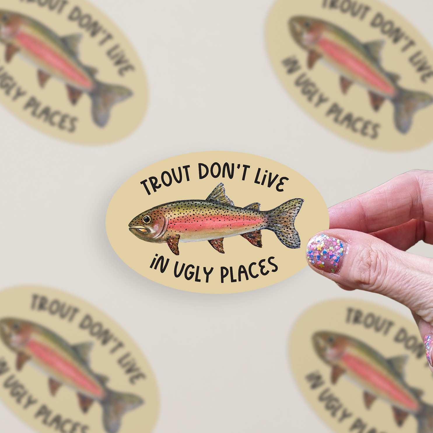 Oval-shaped sticker with a watercolor rainbow trout illustration and the words "trout don't live in ugly places" on a tan background.