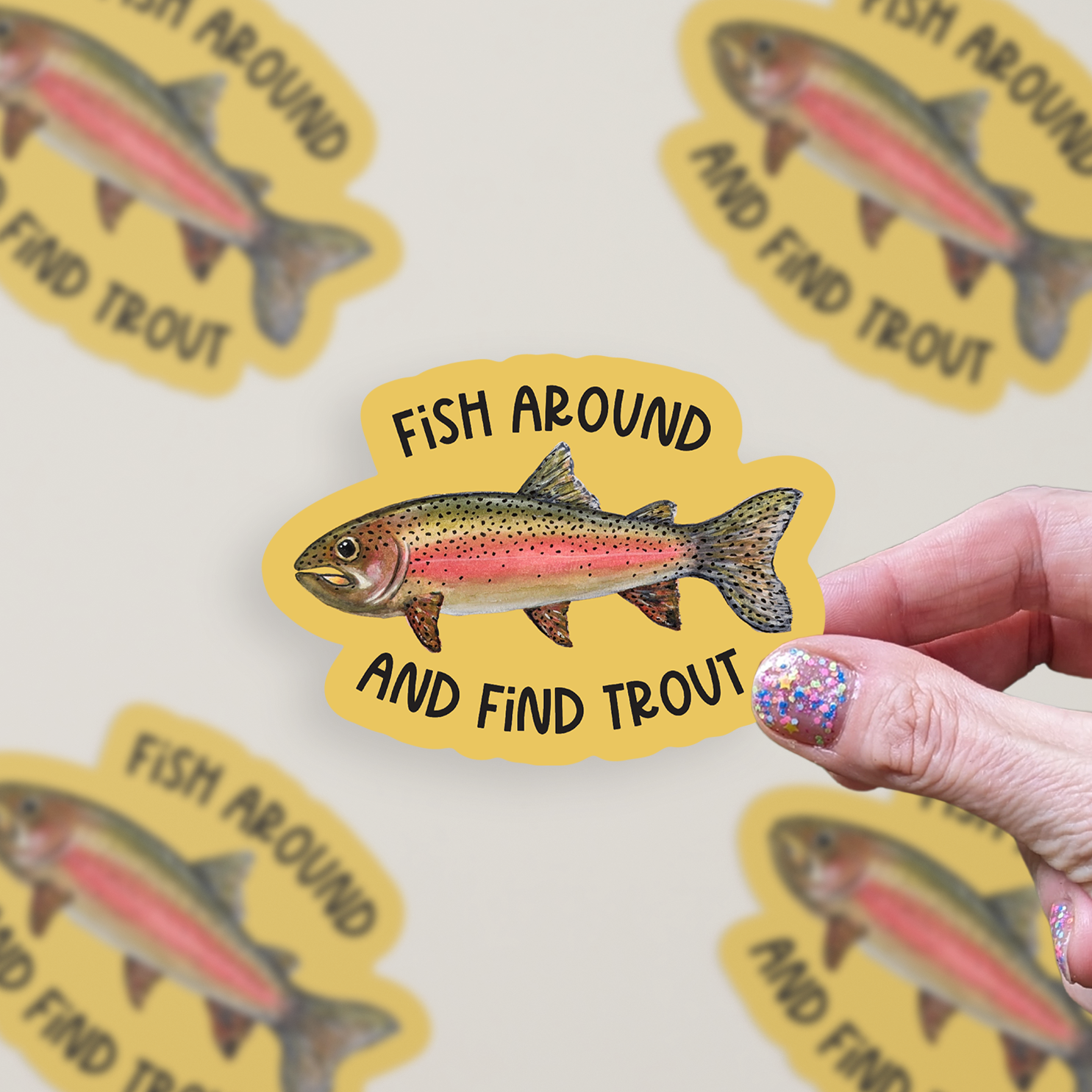 Die cut vinyl sticker with a watercolor rainbow trout illustration on a mustard-colored background with the words "Fish around and find trout"