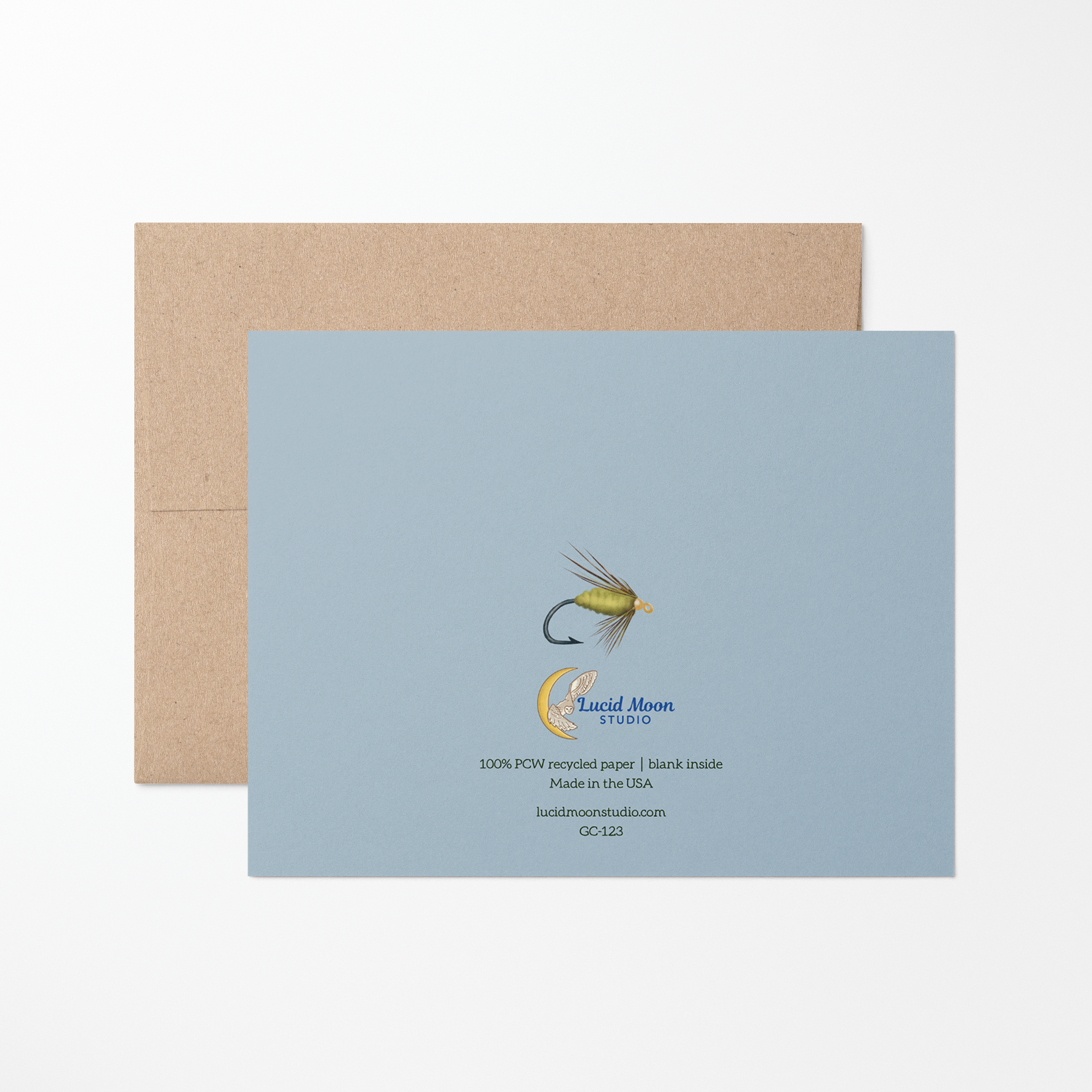 Back of the greeting card with a green fishing fly illustration, Lucid Moon Studio logo, website, and card information on a light blue background with a brown kraft envelope.