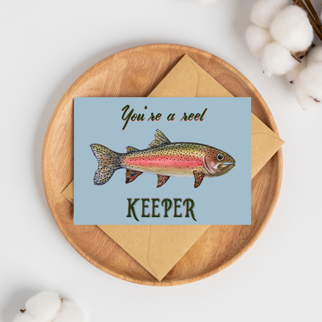 Greeting card with a watercolor rainbow trout illustration and text "You're a reel keeper" on a light blue background with a brown kraft envelope.