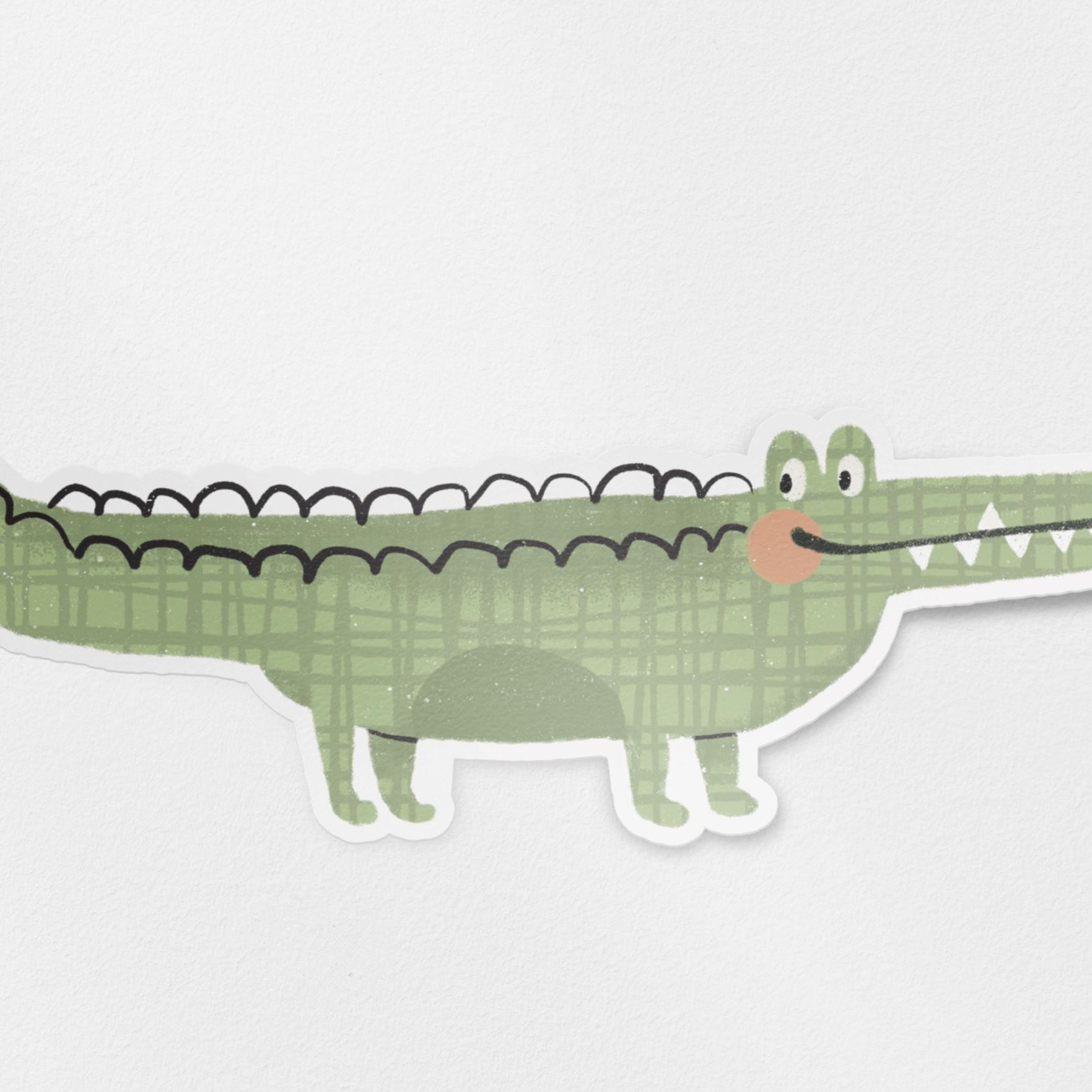 A glossy vinyl die cut sticker with a hand drawn illustration of a cute green crocodile.