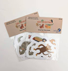 A photo of two packages of six different jungle animal die-cut vinyl stickers that include a toucan, a monkey, a chameleon, a lion, a tiger, and a crocodile in a compostable PLA clear bag with a label describing contents attached.