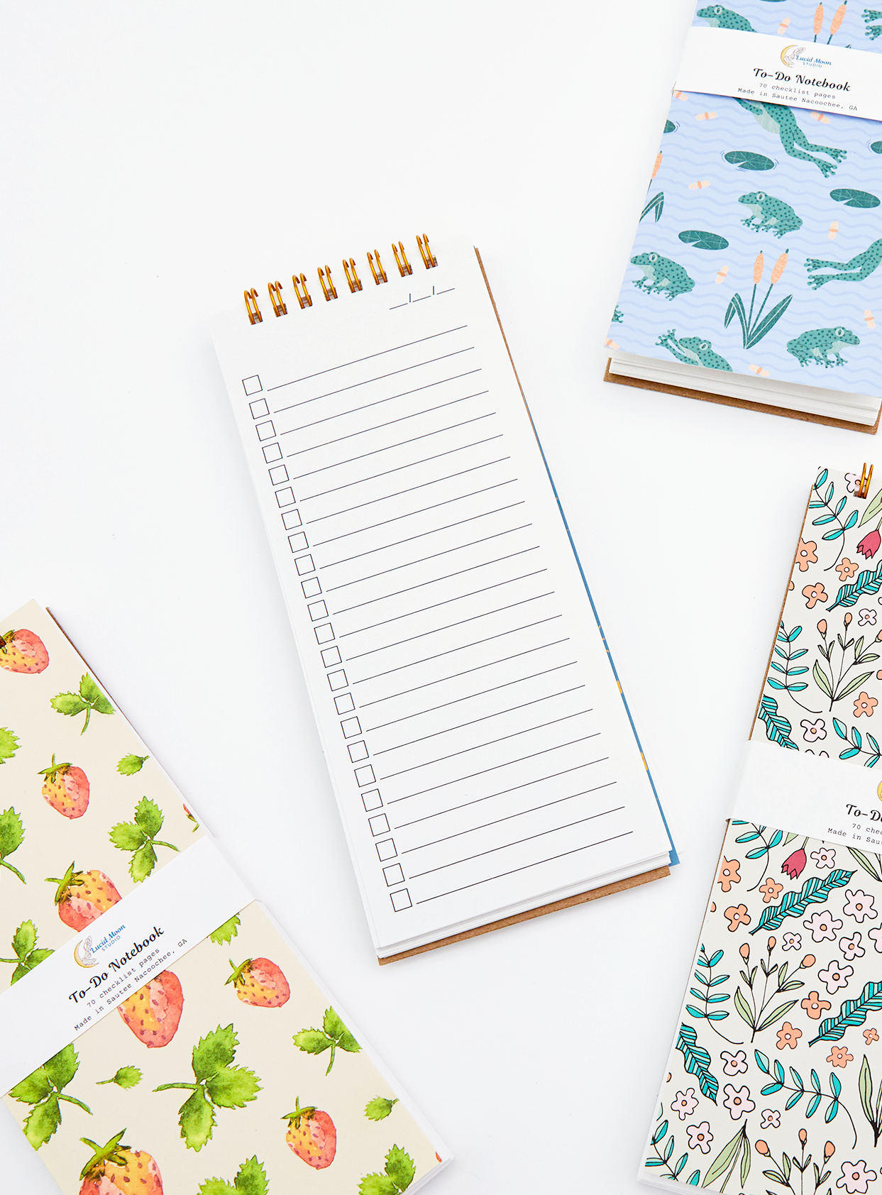 An assortment of spiral notebooks with colorful nature-inspired covers and checklist pages by Lucid Moon Studio