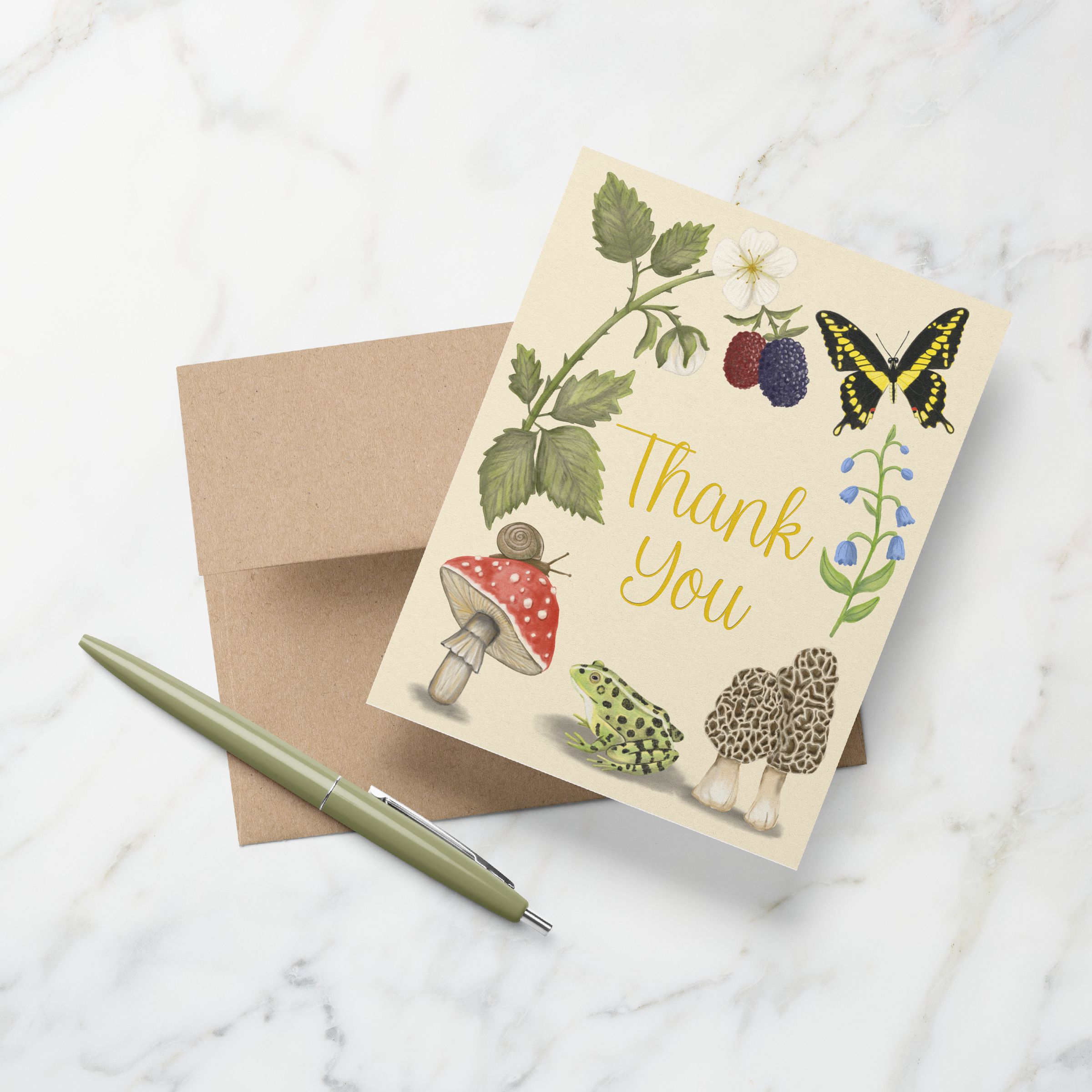 Greeting card with hand-illustrated nature designs and the words Thank You in gold foil on a kraft envelope with a green pen on a marble background