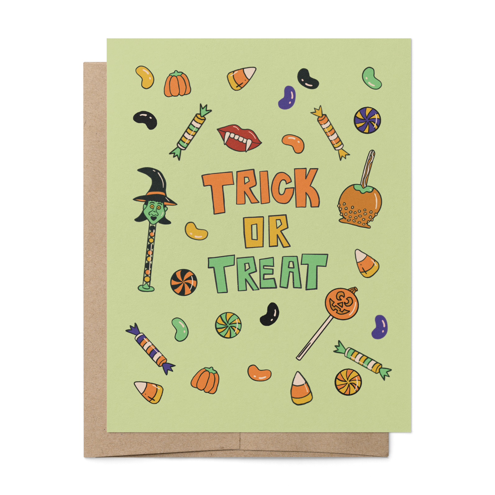 A Halloween greeting card with a light sage green background and 'TRICK OR TREAT' text in orange and green, surrounded by small candy and pumpkin illustrations. A kraft paper envelope is placed behind the card on a white background.