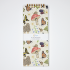 Notebook with nature-themed design featuring mushrooms, butterflies, and flowers on a white background.