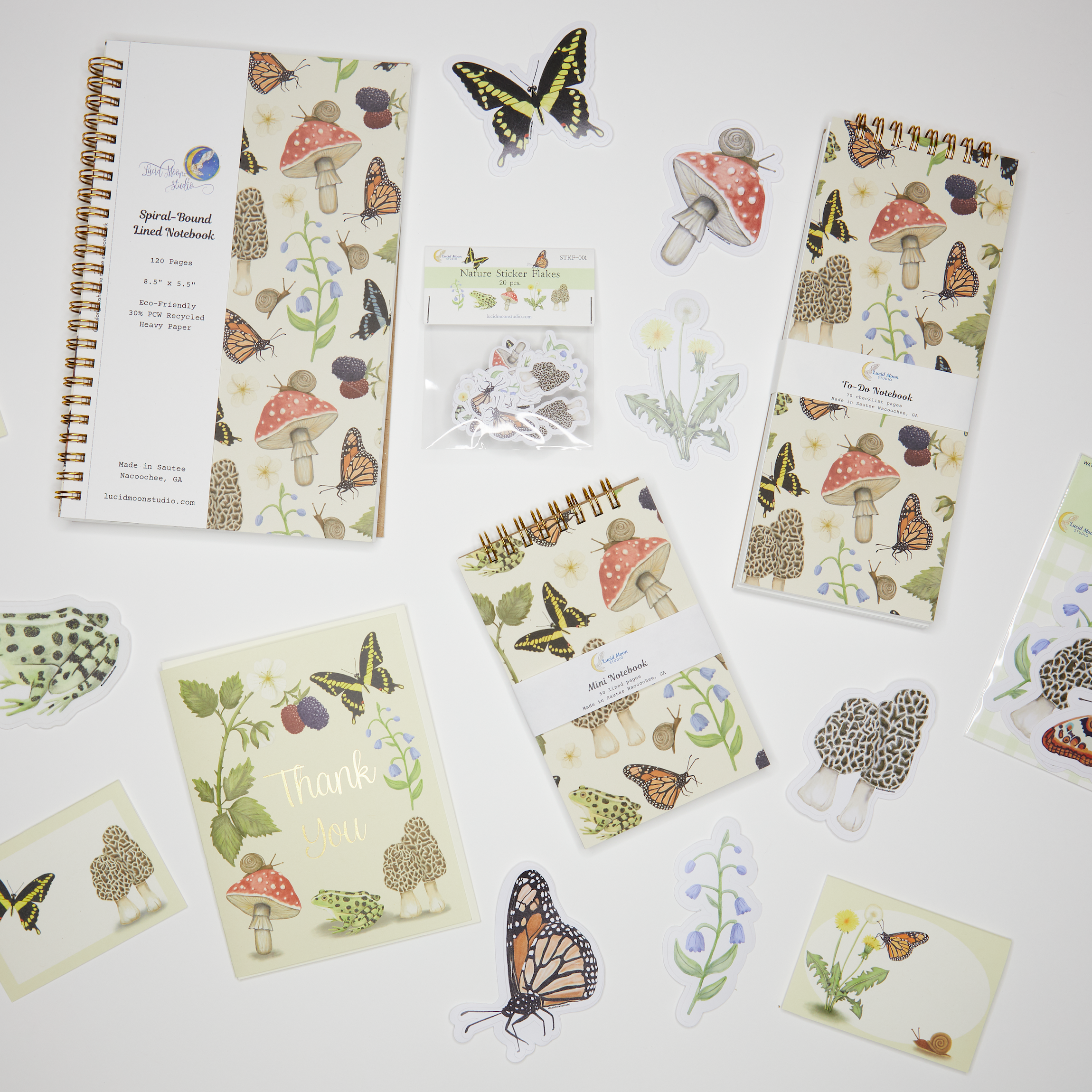 Collection of notebooks and stationery items to include cards, stickers, sticker flakes, and mini note cards with nature-themed designs on a white background.