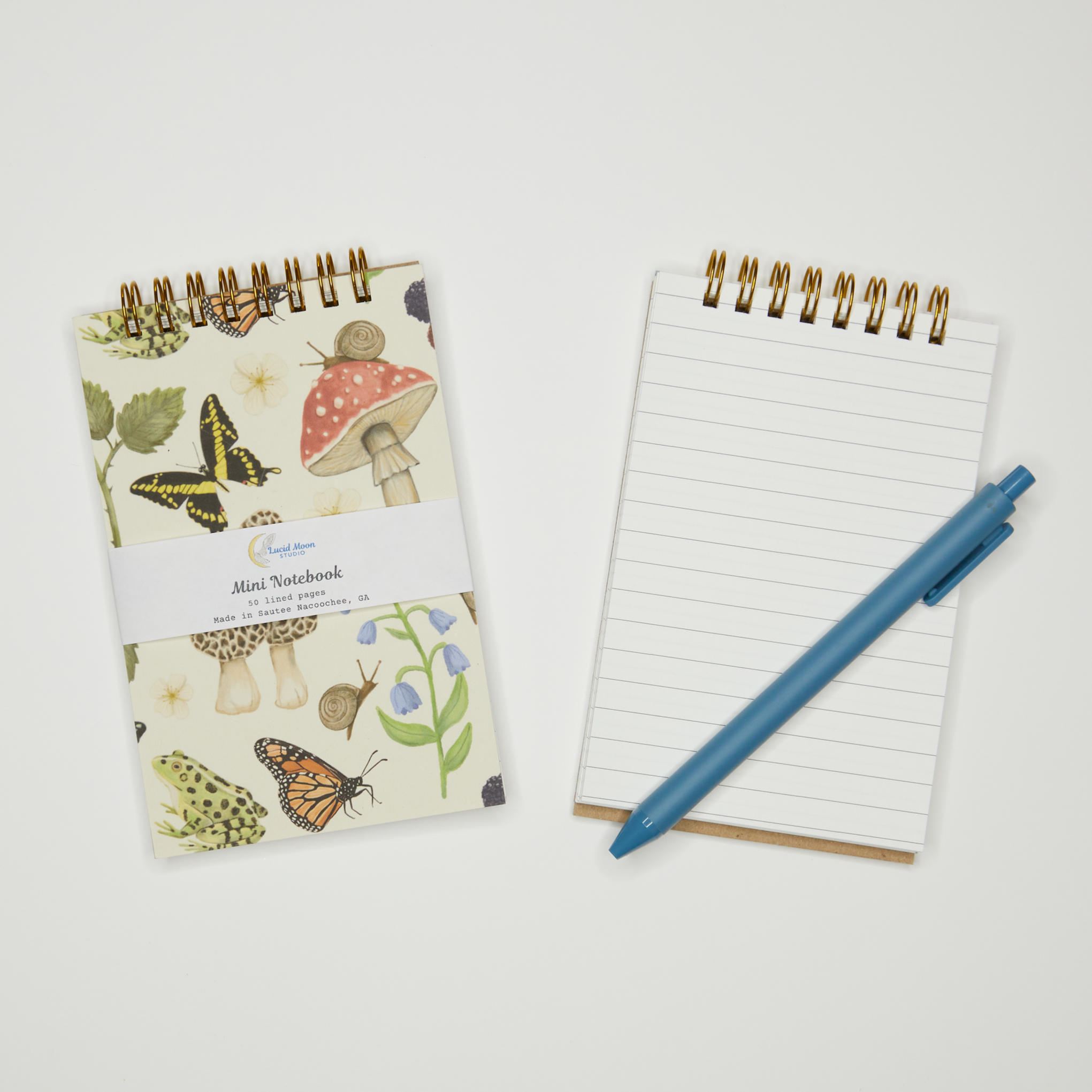 Notebook with butterfly and mushroom design on cover, open to lined pages with a blue pen on a light gray background