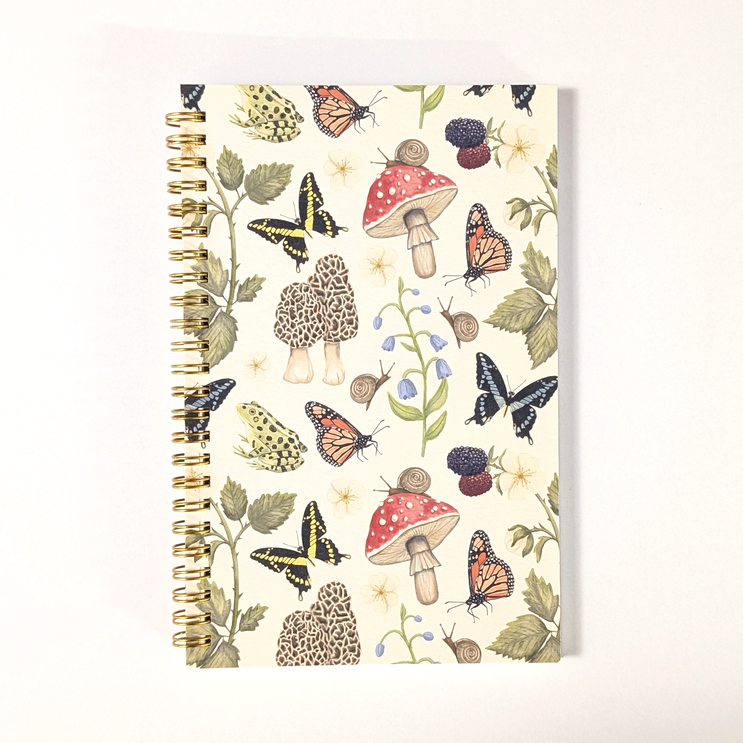 Notebook with nature-themed design featuring mushrooms, butterflies, and leaves on a white background