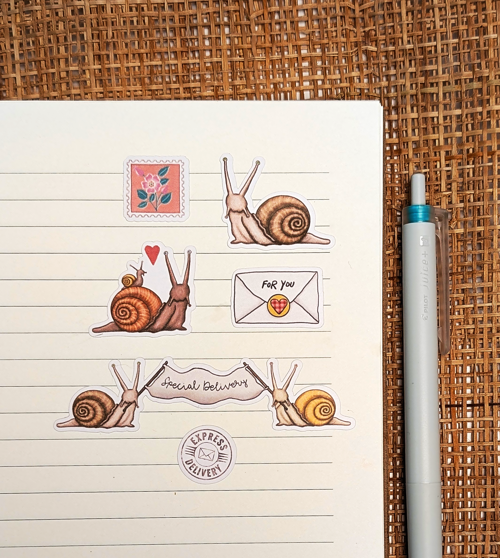 Open notebook with snail mail journal stickers and a pen on a woven surface