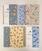 Assortment of spiral notebooks with various colorful patterns and detachable bookmark labels on a white background