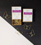 Two boxes of gold butterfly-shaped paper clips are shown on a split black and white background, with several loose butterfly clips scattered around them.