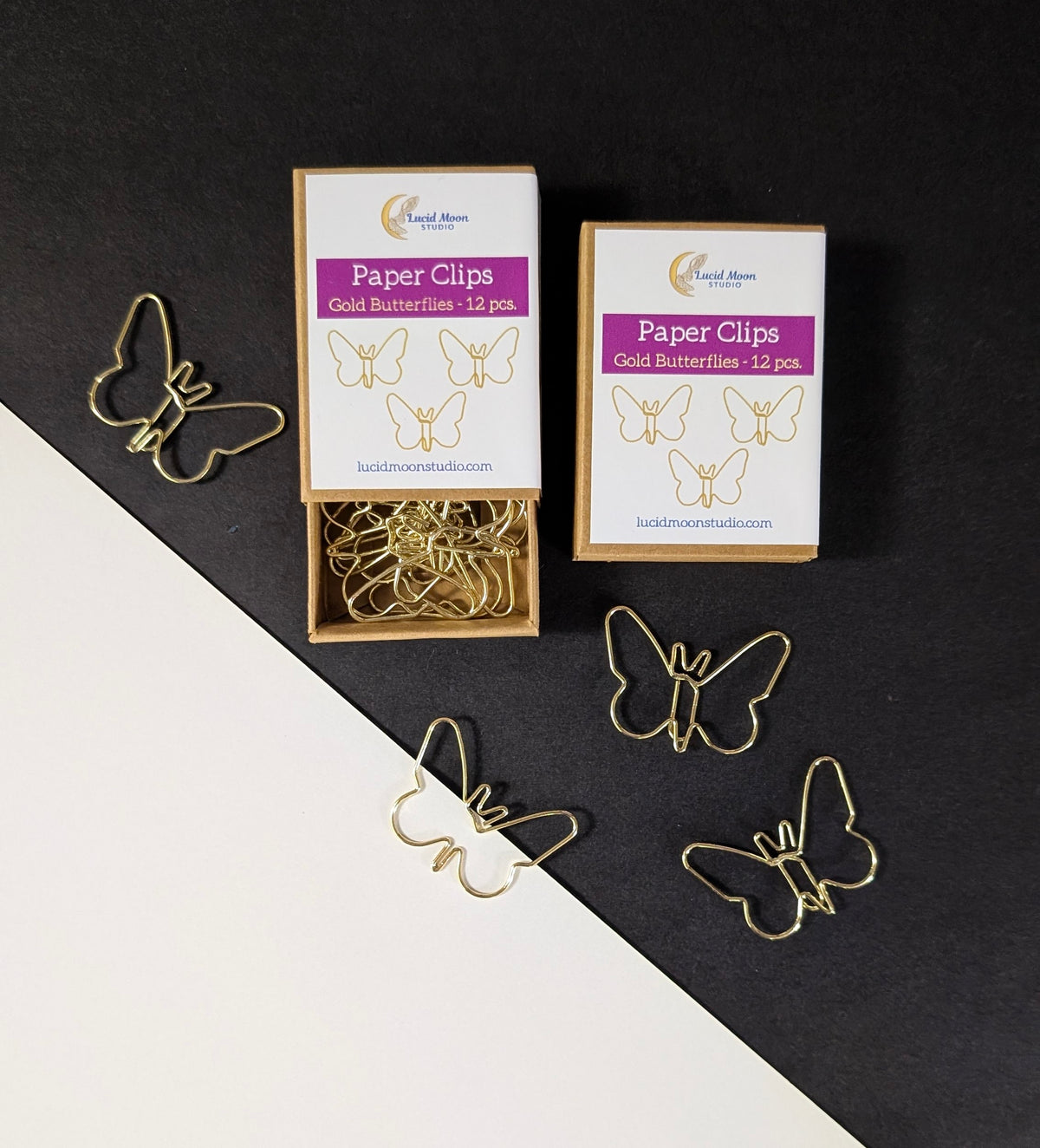 Two boxes of gold butterfly-shaped paper clips are shown on a split black and white background, with several loose butterfly clips scattered around them.
