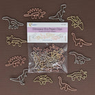 A pack of dinosaur-shaped paper clips arranged around their retail packaging on a solid brown background. The paper clips are made of thin metal wire in various colors including gold, silver, pink, and green, while the packaging is labeled 'Dinosaur Era Paper Clips'.