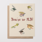 Love/friendship card with 6 fishing fly illustrations and text "You're so FLY!" on a tan background on top of a brown kraft envelope.