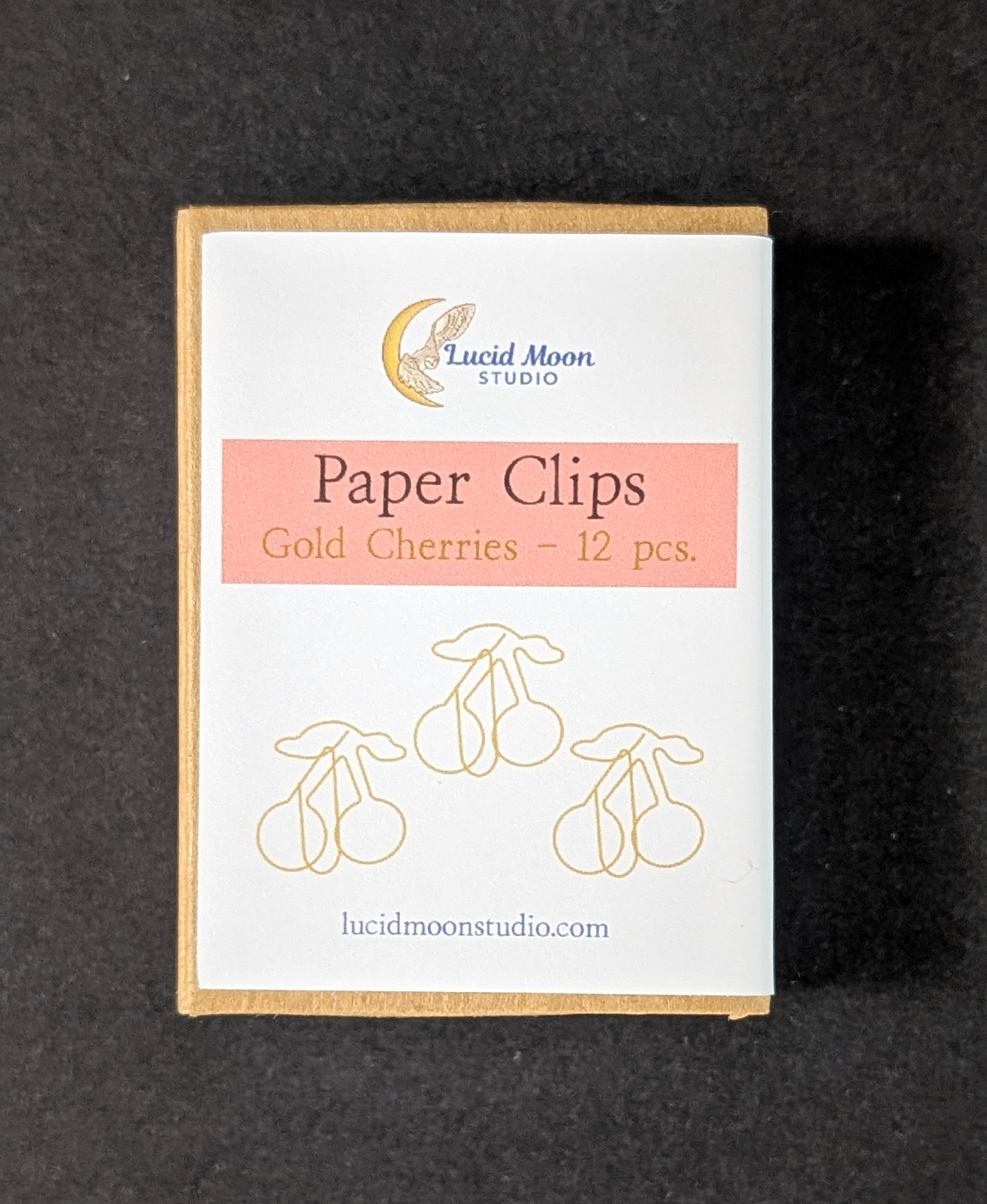 Gold Cherries paper clip set in a kraft paper box with a white label, photographed on a dark textured background.