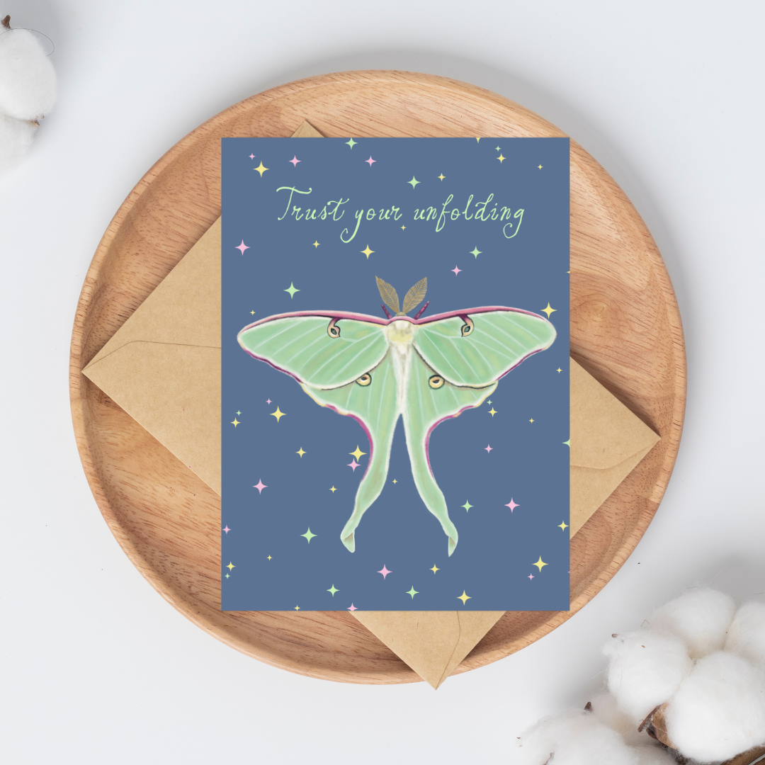 Greeting card with a Luna moth illustration and "Trust your unfolding" text on a blue background with colored stars on it.