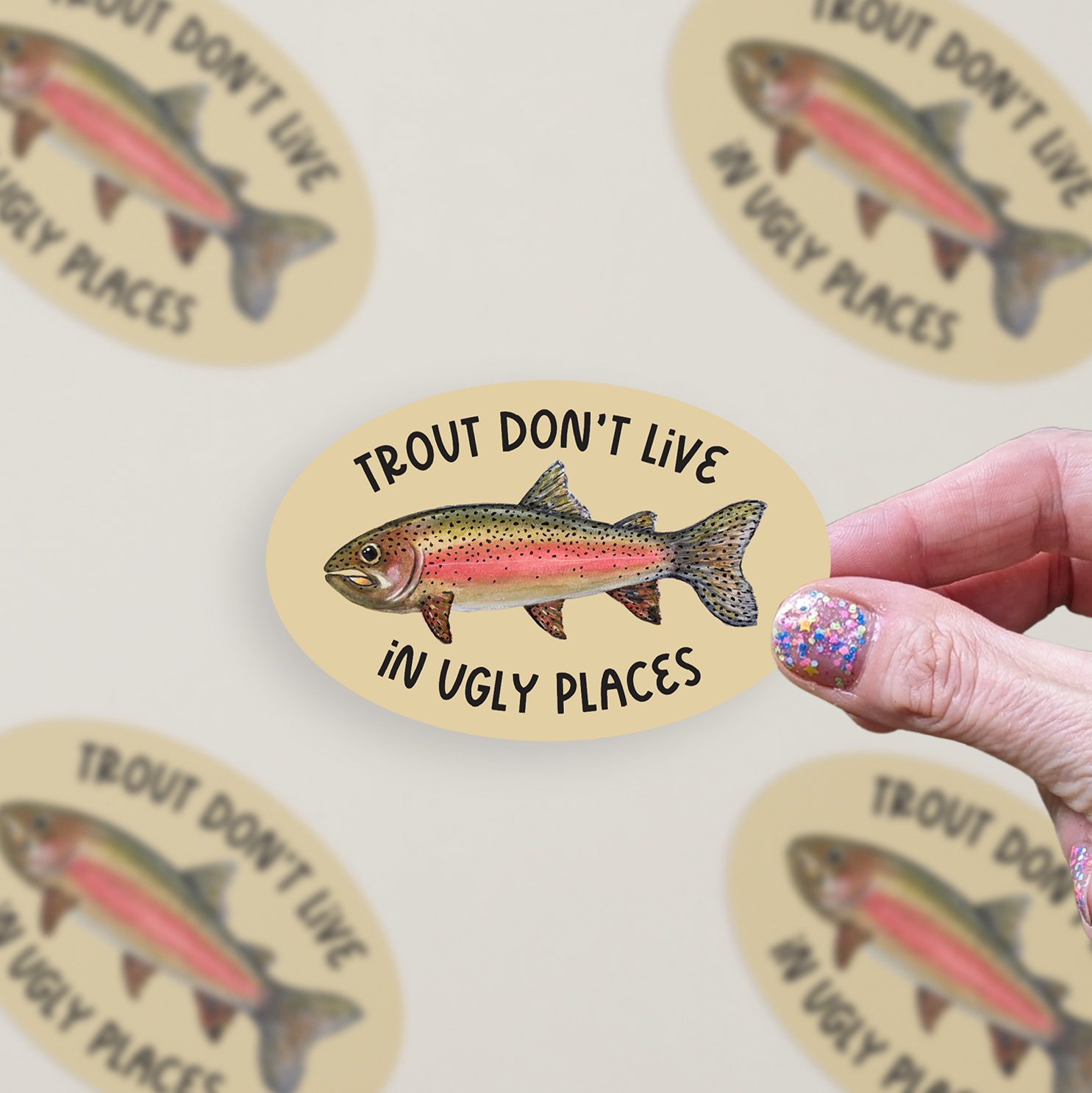 Oval-shaped sticker with a watercolor rainbow trout illustration and the words "trout don't live in ugly places" on a tan background.
