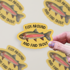 Die cut vinyl sticker with a watercolor rainbow trout illustration on a mustard-colored background with the words "Fish around and find trout"