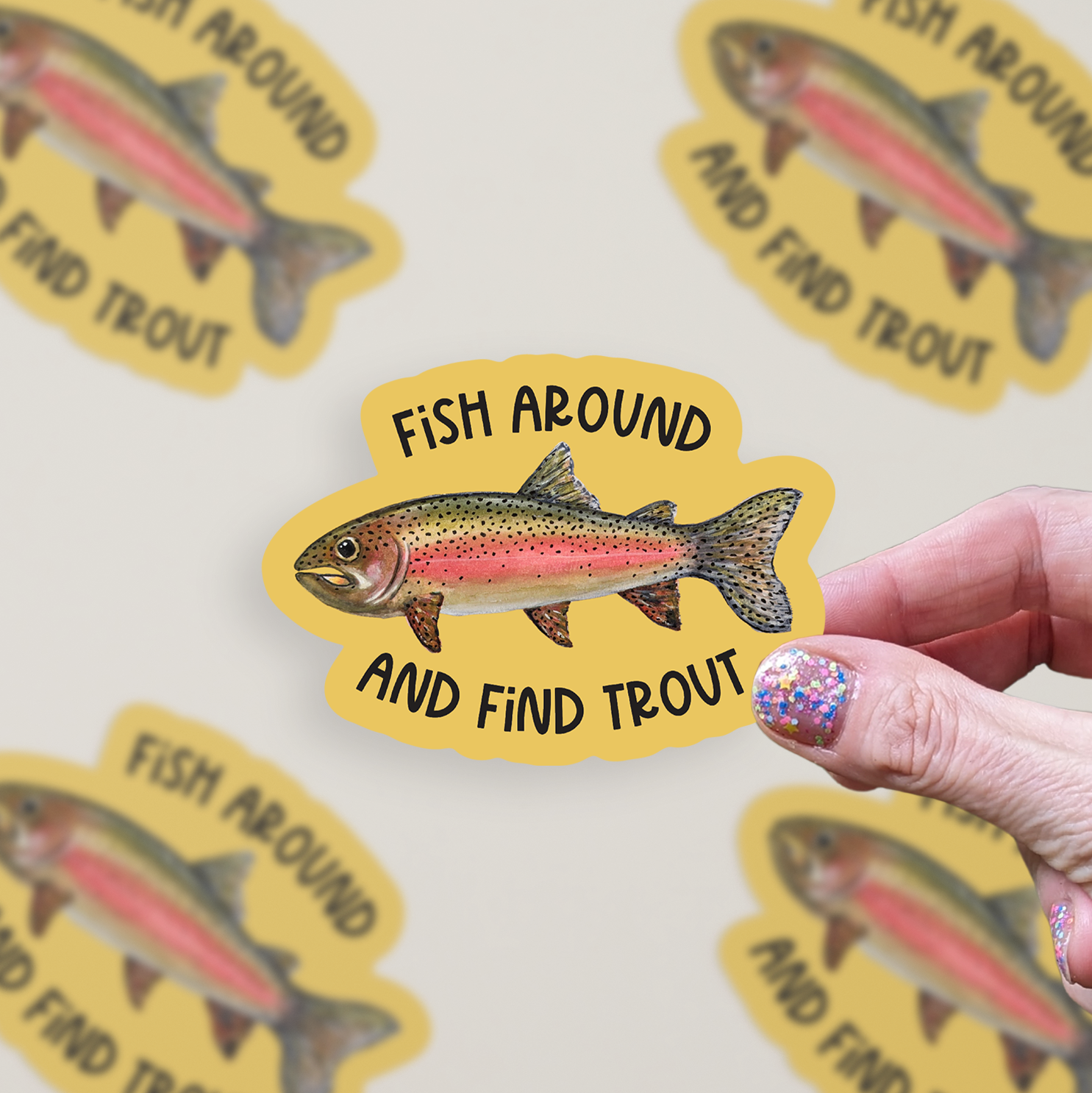 Die cut vinyl sticker with a watercolor rainbow trout illustration on a mustard-colored background with the words "Fish around and find trout"