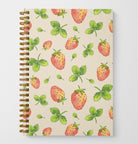 A photo of the front cover of a wire spiral-bound notebook featuring watercolor-painted strawberries and leaves in a tossed pattern.